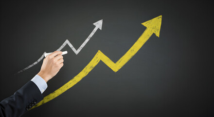 Hand drawing a large yellow upward arrow over a white upward arrow on a blackboard, symbolizing accelerated business growth and strategic improvement.