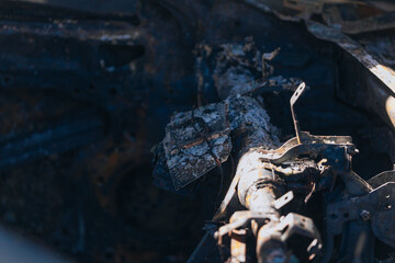 Burnt carcasses covered in ash and mud show twisted metal and melted structures. Destroyed car interior. Consequences of military conflict and shelling. Destroyed parking lot.