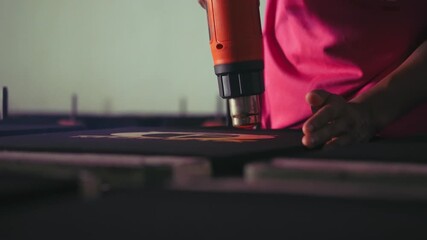 a man drying screen printing paint on the surface of a cloth using a heatgun