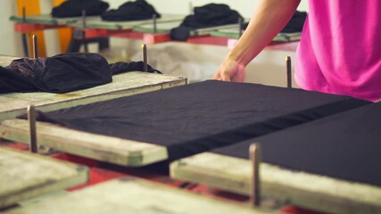 a man attaching a black T-shirt to a screen printing table for printing.