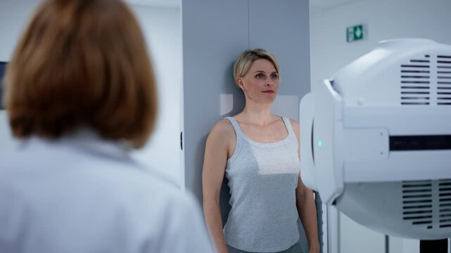 Female patient undergoing dynamic X-ray scan using tilting fluoroscopy wall unit.