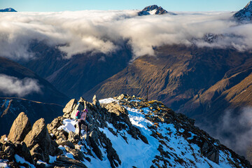 Brave hiker girl scrambles along very narrow rocky ridge on way to Avalanche Peak summit. Breathtaking mountain views in Arthur's Pass National Park, Canterbury, South Island, New Zealand.