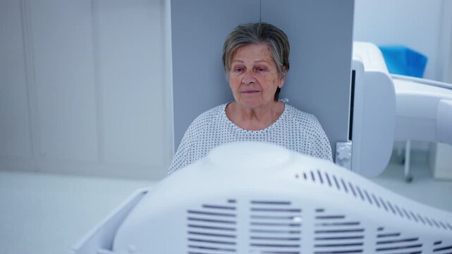 Senior female patient undergoing dynamic X-ray scan using tilting fluoroscopy wall unit.