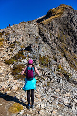 Brave hiker girl climbs steep rocky vertical wall on way to Avalanche Peak summit, Arthur's Pass National Park, Canterbury, South Island, New Zealand