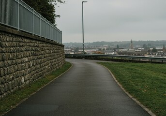 Obraz premium Curving pathway alongside a stone wall with a distant cityscape.