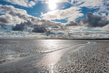 Dramatisch aufgebauschte Wolkenberge bei stürmischem Wetter über dem glitzernden Watt auf der Nordseeinsel Föhr im Gegenlicht der Sonne
