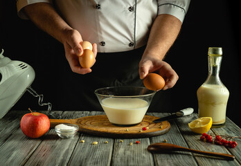 A chef skillfully cracks eggs into a glass bowl filled with milk, while a fresh apple, salt, lemon, and olive oil surround the workspace. The kitchen atmosphere is warm and inviting