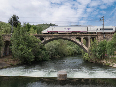 Ponferrada, Leon, Spain; 06-15-2025: The Renfe Alvia train of the Spanish public operator Renfe Viajeros enters Ponferrada station, passing over a bridge and leaving its reflection in the Sil River