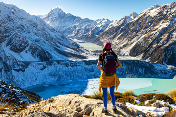Hiker girl climbs snow-covered stairs on Sealy Tarns Track, admiring alpine views of Aoraki Mount Cook and surrounding glacial lakes, South Island, New Zealand