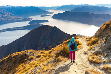 Hiker girl hikes along Roys Peak trail and admires stunning panoramic views over Lake Wanaka and surrounding alpine peaks near Wanaka, Otago, South Island, New Zealand.