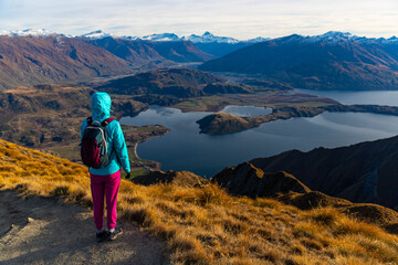 Hiker girl hikes along Roys Peak trail and admires stunning panoramic views over Lake Wanaka and surrounding alpine peaks near Wanaka, Otago, South Island, New Zealand.