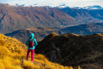 Hiker girl hikes along Roys Peak trail and admires stunning panoramic views over Lake Wanaka and surrounding alpine peaks near Wanaka, Otago, South Island, New Zealand.