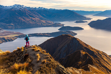 Adventurous hiker girl stands on summit of Roys Peak  admiring breathtaking panoramic view over Lake Wanaka and surrounding snow covered peaks near Wanaka, Otago, South Island, New Zealand © Lens Down Under