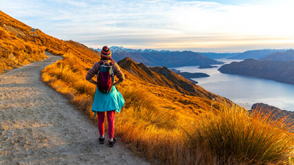 Adventurous hiker girl stands on summit of Roys Peak admiring breathtaking panoramic view over Lake Wanaka and surrounding snow covered peaks near Wanaka, Otago, South Island, New Zealand