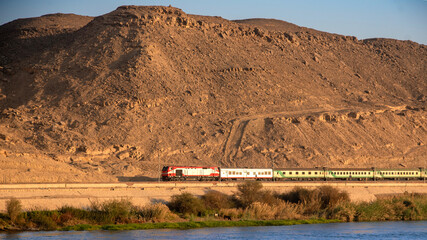 Train traveling between the Nile River and a desert mountain near Aswan, Egypt - a stunning...