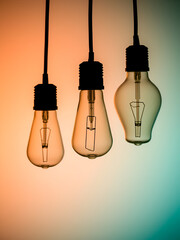Three classic light bulbs, varying in transparency, shine subtly on a gradient backdrop transitioning from teal to orange, symbolizing enlightenment and clarity.