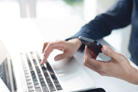 Business woman using smartphone and working on laptop computer with digital tablet on office table. Businesswoman surfing the internet, web browsing via laptop and searching the information, closeup