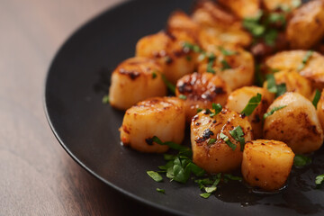 roasted scallops with baked potatoes wedges on a black plate on walnut wood background