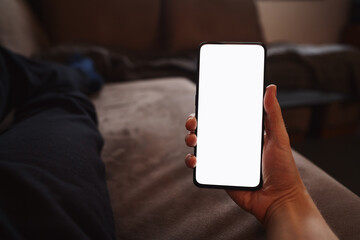 Man hold smartphone with white screen in his hand lying on a couch in home environment