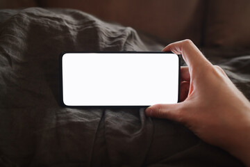 man hand holding phone with white screen over bed on background
