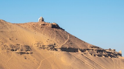 Ancient rock-cut Tombs of the Nobles on the hillside across the Nile River from Aswan, Egypt, seen from the riverbank.