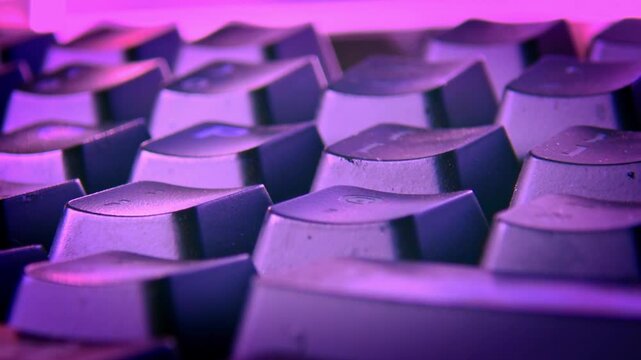 Camera pulls back from computer keyboard in purple light