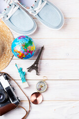 Travel planning simple background of compass, film camera, straw hat, moccasins, globe and souvenirs on white planks flat lay with copy-space