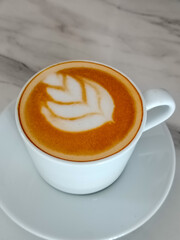 cup of hot coffee latte with leaf latte art on marble table in minimal white ceramic mug and saucer.