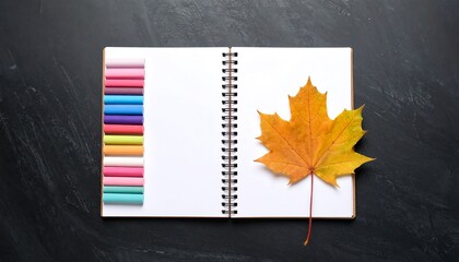 Open notebook with blank pages, maple leaf and colourful pastel chalk on black background