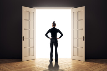Fototapeta premium Woman standing in dark room facing open door filled with bright white light, symbolizing opportunity and new beginnings in career and life.