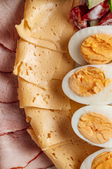 Close-up of a classic breakfast platter featuring sliced cheese, ham, hard-boiled eggs, and a fresh vegetable salad. Perfect for brunch, catering, or healthy meal concepts.