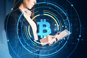 Businesswoman using tablet with glowing bitcoin symbol overlay and digital network graphics on dark background, representing cryptocurrency concept.