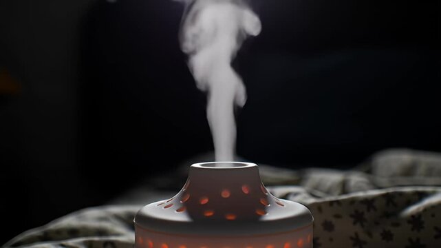 Aroma diffuser emitting steam, lit from within, sits on a patterned blanket in the dark