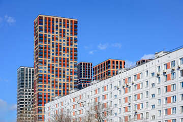 Modern high-rise residential buildings and older apartment block under clear blue sky. Urban contrast of contemporary architecture and traditional housing. Real estate and city development concept. © SSV-Photo