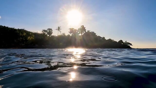 Sunset over smooth ocean waves with coconut palm trees in Amed on tropical island of Bali Indonesia