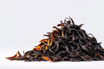 Obraz premium Black tea leaves piled on a white background showcasing their rich color and texture, highlighting natural aromas and flavors for an enticing beverage experience