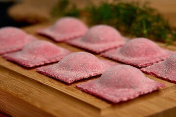 Artisanal Pink Ravioli on Wooden Board Surrounded by Fresh Herbs and Accents of Flour Ready for Cooking and Culinary Exploration in a Rustic Kitchen Environment