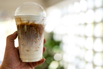 Layered iced caramel macchiato in plastic glass on hand
