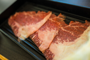 Raw beef for shabu shabu on a black plate. Close up
