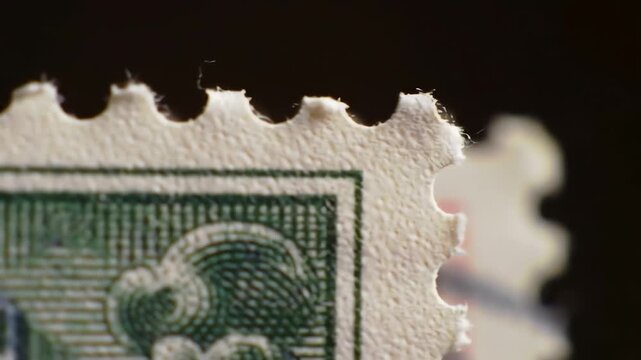 Close-up of a vintage postage stamp with perforated edges and an intricate green design, with another postage stamp on a dark background behind