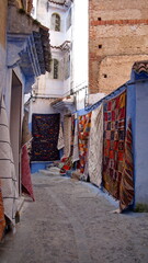 Colorful textiles hanging on a blue wall in an alley in the medina in Chefchaouen, Morocco