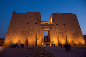 Temple of Edfu illuminated at dawn - golden lights highlight the ancient structure as the sky transitions from night to day in Edfu, Egypt.