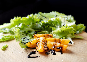 Sliced tomatoes drizzled with sauce and sprinkled with sesame seeds on a wooden cutting board. Close-up of tomatoes and lettuce. Concept of healthy eating and organic farm products
