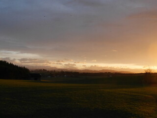 Beautiful sunset over a field with a small house in the distance