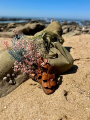 sandals, bag, flowers stacked near a rock on the beach in summer