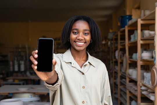 Woman showing smartphone screen in pottery studio for online sales and marketing