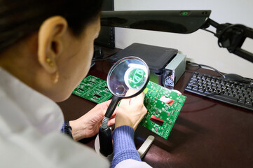 Expert technician examines circuit boards under magnifying glass in a modern electronics workshop