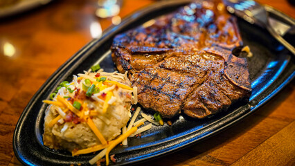 juicy grilled T bone steak, perfectly seared, served alongside a loaded baked mash potato on a warmly lit rustic dining setup. Ideal for culinary content