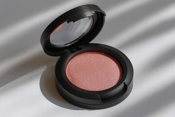 Close up of a single round compact of shimmering peachy pink eyeshadow with a black lid casting subtle shadows