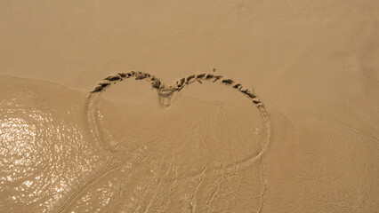 Heart shape on sand were deleted by water from the sea